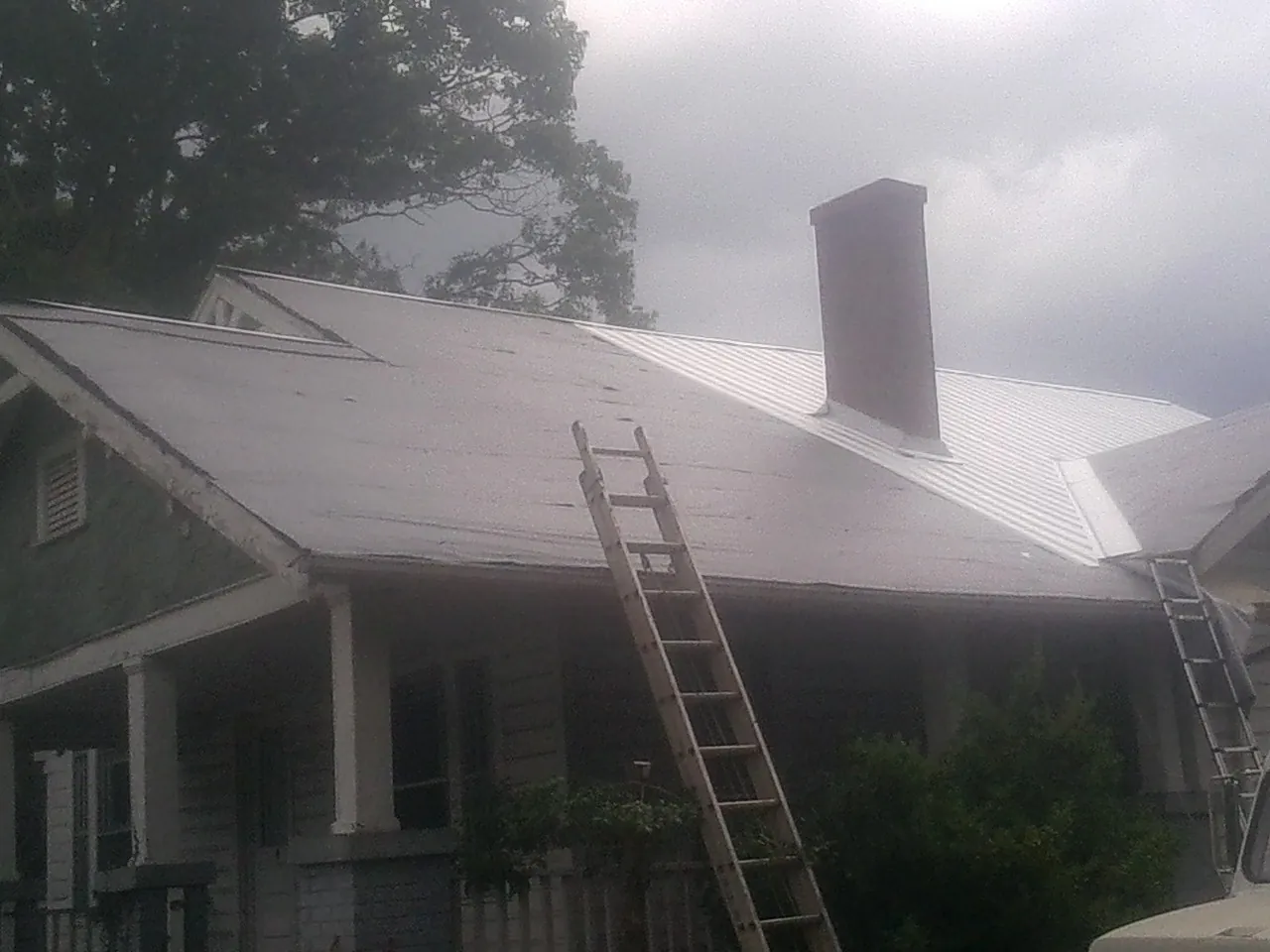 Ladders against a metal roof on an older home with a brick chimney in Caledonia